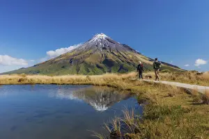 Two Persons Prints: Two tourists hiking at Taranaki volcano in New Zealand northern island reflecting in a