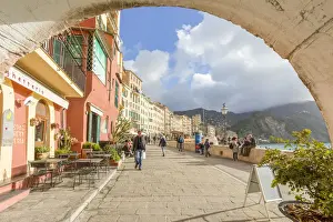 Tourists walking on the picturesque promenade of Camogli framed with an old arch
