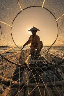 Traditional fisherman viewed through conical fishing net collecting fish on a boat
