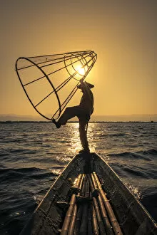 Traditional leg-rowing fisherman posing with conical fishing net on a boat on Lake Inle