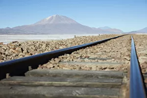 Salt Flat Collection: A train track on the Bolivian plateau with the OllagAoe volcano in the background