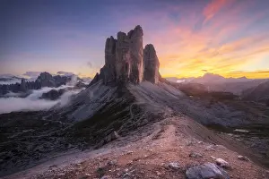 The Tre Cime di Lavaredo lined up from the Forcella Lavaredo during a cold late summer sunset, with the Cadini di Misurina emerging from the fog on the left. Dolomites, Italy