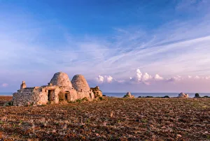 Bari Province Prints: Trulli during the sunrise in a dry field with the sea on the background, Polignano a Mare