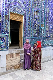 Uzbekistan, Samarkand, Shah-i-Zinda, Tomb Street of 11 Mausoleums, two young women with a baby stand in front of the entrance to a mausoleum