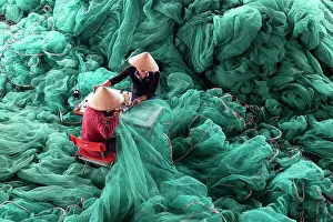 Vietnam, Cam Ranh, two men repair green fishing nets using a sewing machine