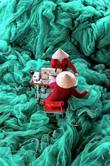 Vietnam, Cam Ranh, women mend green fishing nets using a sewing machine