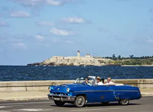 Vintage car at El Malecon with El Morro Castle and Lighthouse in the background, Havana