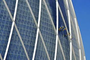 Window cleaners hanging on The Coin building Aldar headquarters, one of the largest