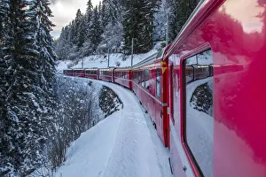 The windows of the red train reflecting the landscape of snowy woods of Sankt Moritz