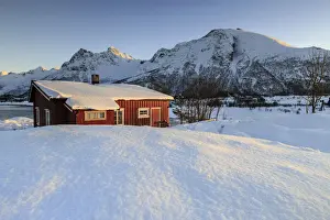 The winter sun illuminates a typical Norwegian red house surrounded by fresh snow