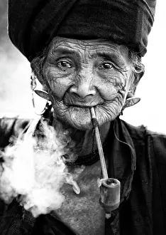 B And W Prints: Woman of the Ann tribe in traditional black dress smoking a pipe outside a hill village near Kengtung (Kyaingtong)