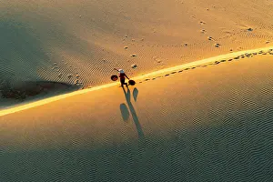 Dune Prints: Woman with basket on golden dunes at dawn, Nam Cuong, Ninh Thuan Province, Vietnam. (MR)