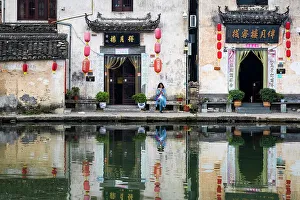 Bench Prints: Woman on bench and village buildings reflected in pond, Hongcun, China