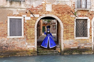 Mediterrranean Prints: A woman in a blue costume stands by a canal during the Venice Carnival, Venice, Italy