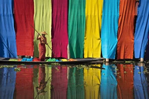 Burmese Gallery: Woman on a boat checking freshly dyed fabric hanging from bamboo poles to dry