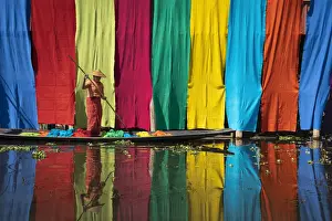 Women Prints: Woman on a boat checking freshly dyed fabric hanging from bamboo poles to dry