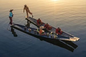 A woman on a boat giving rice as alms to three monks sitting on a boat at sunrise