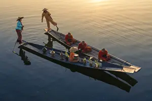 Robes Prints: A woman on a boat giving rice as alms to three monks sitting on a boat at sunrise