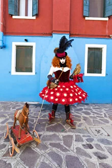 Images Dated 29th March 2018: A woman in a colourful costume poses with a toy dog in a street on Burano Island during