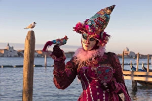 Woman in costume holding a bird at Carnival time and gull on post, Lagoon, Venice
