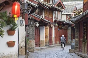 Woman cycling along alleyway, Lijiang (UNESCO World Heritage Site), Yunnan, China