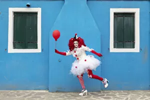 Images Dated 17th March 2020: A woman dressed as a clown holds a ballon in front of a colourful facade on Burano