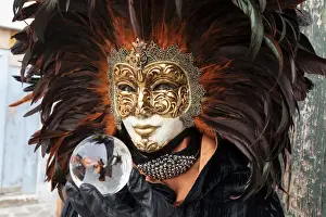 Eyes Prints: A woman in a feather Venetian mask poses with a glass ball during the Venice Carnival