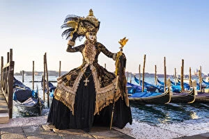 Images Dated 10th February 2018: A woman in a magnificent costume poses in front of Gondolas during the Venice Carnival