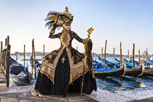 A woman in a magnificent costume poses in front of Gondolas during the Venice Carnival