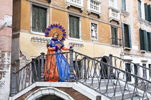 Woman in orange and blue costume at Carnival time on bridge over canal, Venice, Veneto