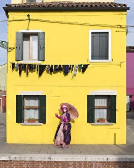 Woman in pink costume holding umbrella in front of yellow house during Carnival, Island