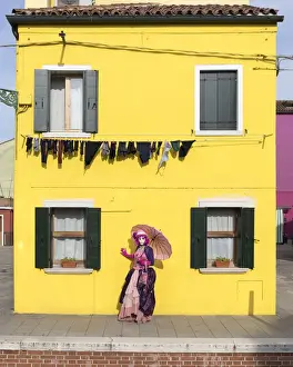 Washing Prints: Woman in pink costume holding umbrella in front of yellow house during Carnival, Island