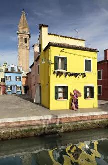 Woman in pink costume posing in front of yellow house during Carnival, Island of Burano