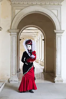 A woman in a red costume and mask poses in an archway during the Venice Carnival A woman in a red costume and mask poses in an archway during the Venice Carnival