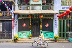 A woman rides a bicycle past buildings in Hoi An Ancient Town, Hoi An, Quang Nam Province
