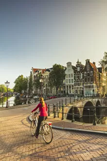 A woman riding a bike on a bridge over a canal in Amsterdam at sunset