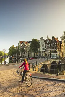 Bicycle Gallery: A woman riding a bike on a bridge over a canal in Amsterdam at sunset