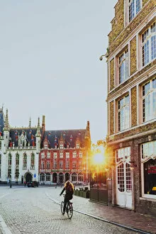Bikes Collection: A woman riding a bike in Bruges Market Square at sunrise, Belgium