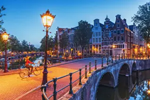 A woman riding a bike by night in Amsterdam along Keizersgracht canal in Amsterdam