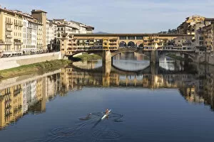 A woman rows on the Arno river towards the Ponte Vecchio, Florence, Tuscany, Italy