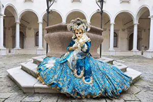 A woman sits in a magnificent costume in front of a well during the Venice Carnival