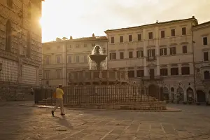 Woman walking past Fontana Maggiore in Piazza IV Novembre at dawn Perugia, Umbria, Italy