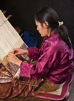A woman weaves an intricate pattern in silk on her traditional wooden loom