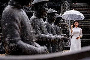 Model Released Prints: Woman in white ao dai by statues with umbrella, Khai Dinh Mausoleum, Hue, Vietnam. (MR)