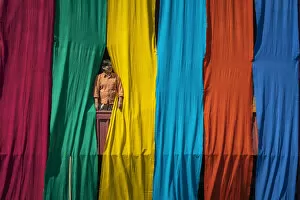 Images Dated 23rd April 2020: Woman in a window checking freshly dyed fabric hanging from bamboo poles to dry on a