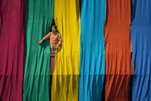 Images Dated 23rd April 2020: Woman in a window checking freshly dyed fabric hanging from bamboo poles to dry on a