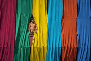 Women Prints: Woman in a window checking freshly dyed fabric hanging from bamboo poles to dry on a