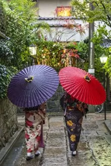 Women in traditional dress with umbrellas walking through Kyoto, Japan