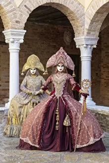 Two women wearing Indian style costumes and masks pose in the cloisters of Chiesa di San