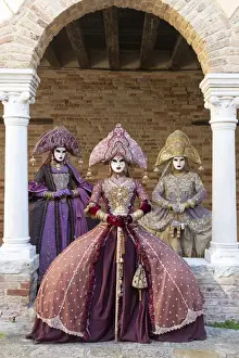 Three women wearing Indian style costumes and masks pose in the cloisters of Chiesa di